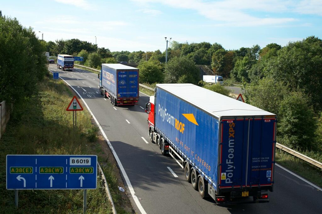 Cargo trucks on A38 highway, Mansfield, UK, surrounded by summer greenery and clear skies.